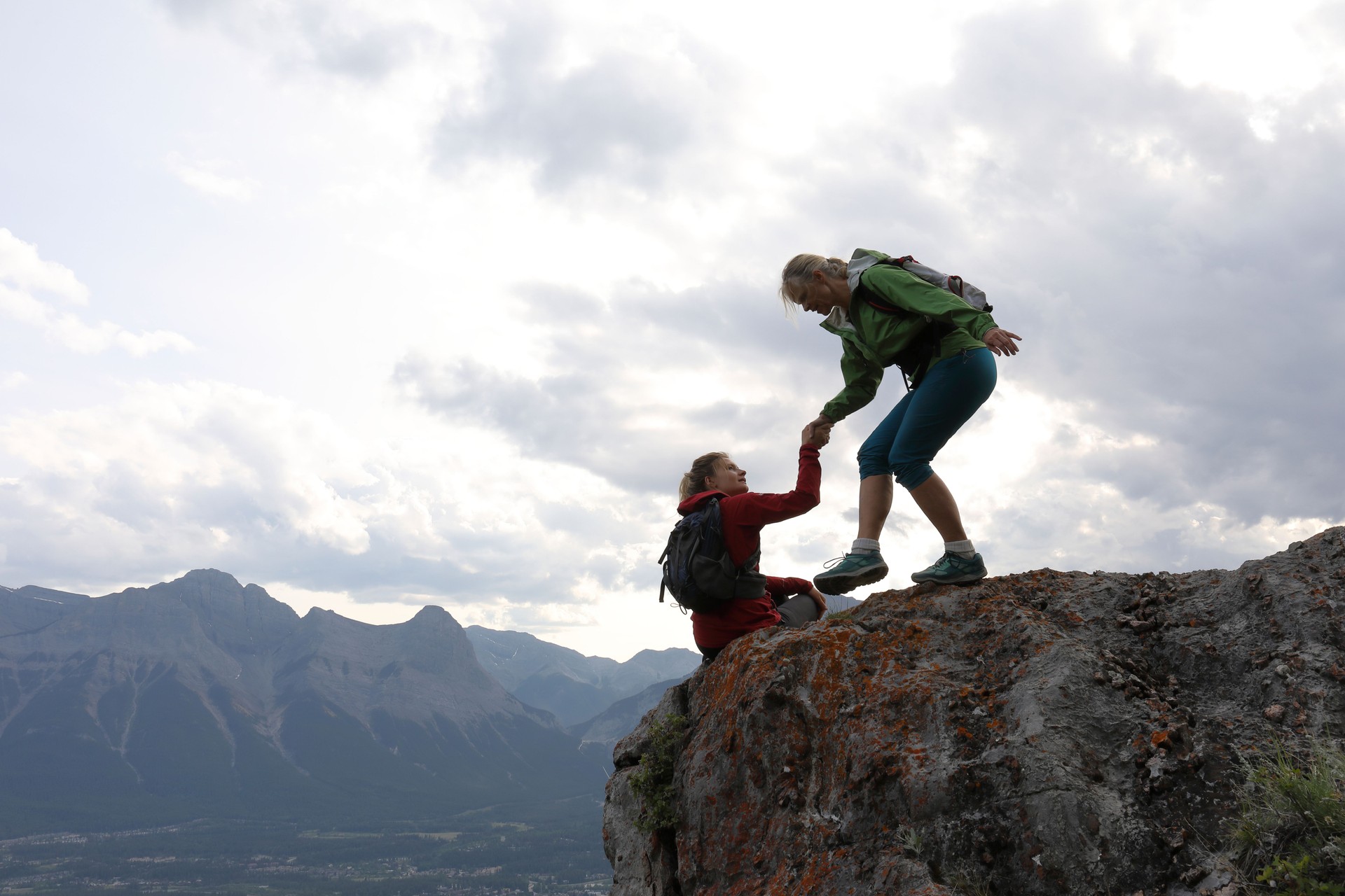 Female climbers helping each other up a mountain